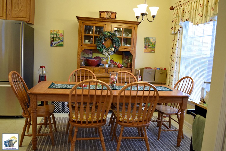 Yellow kitchen with a oak farmhouse table and a gray and white striped rug decorated for the holidays