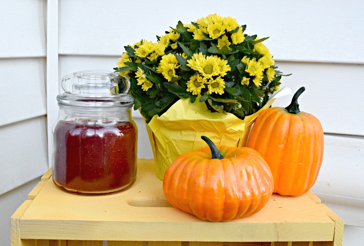 Fall front porch decor with a candle, crate, mums and pumpkins