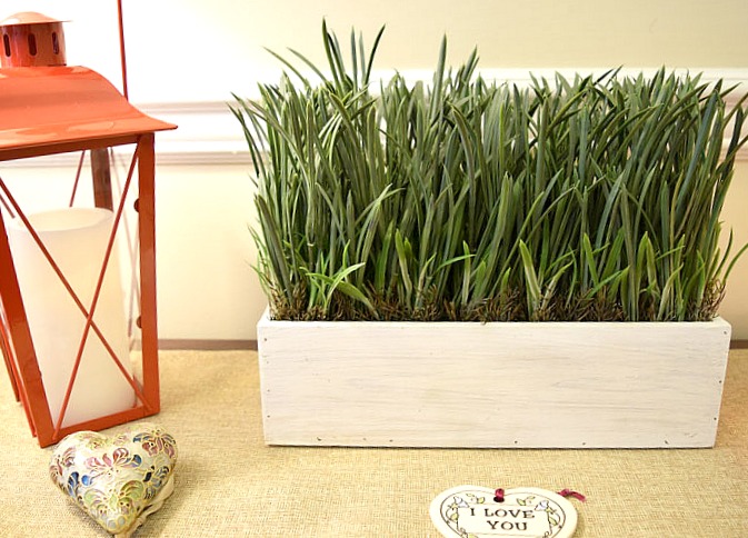 console table with red lanterns, heart ornaments and faux grass in a white rectangular planter
