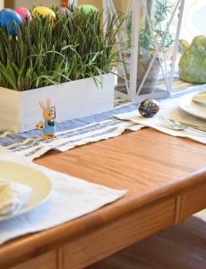 A beautiful farmhouse-style table decorated for Easter with a faux grass and Easter egg centerpiece