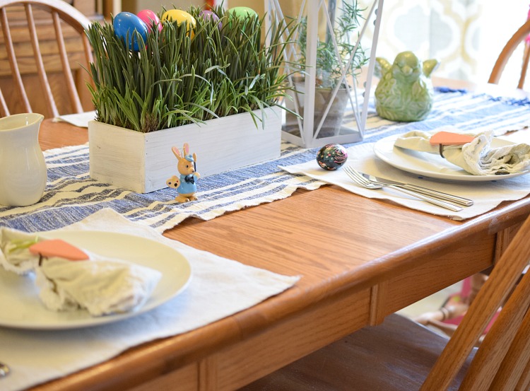 A beautiful farmhouse-style table decorated for Easter with a faux grass and Easter egg centerpiece