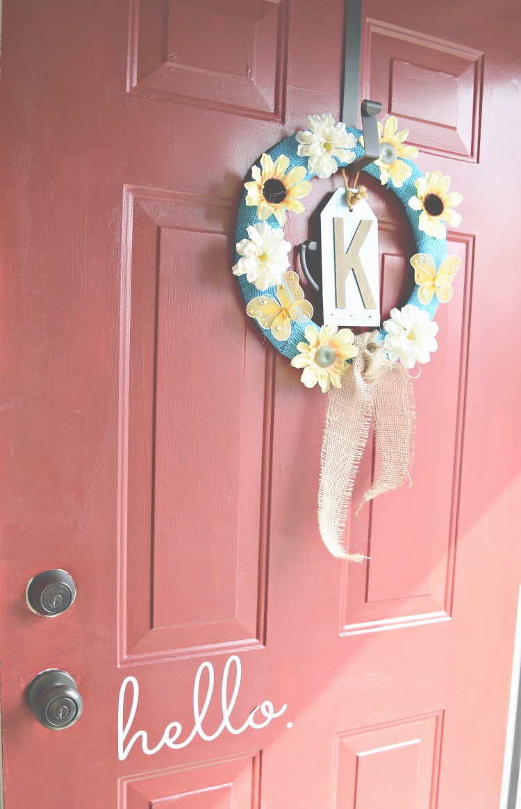 Blue burlap wreath with yellow faux flowers and butterflies on a red front door with the word "hello" and a K monogram