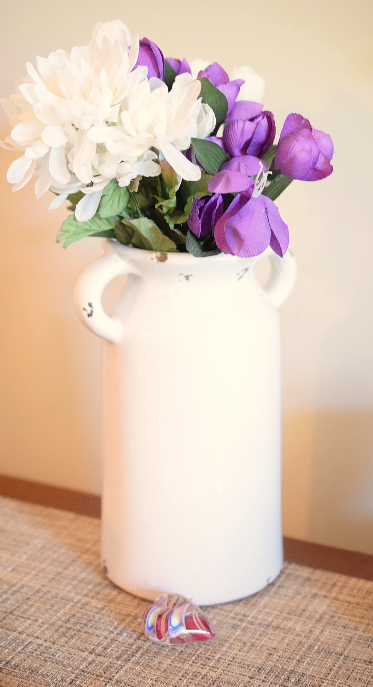 faux purple and white flowers in a chipped white farmhouse style vase