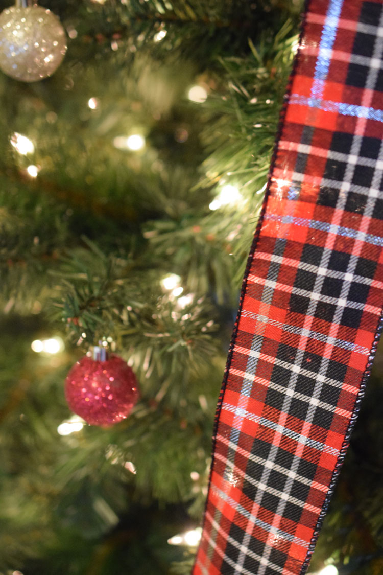 Red, white and black plaid ribbon on a faux pine Christmas tree with a glittery red ball orament