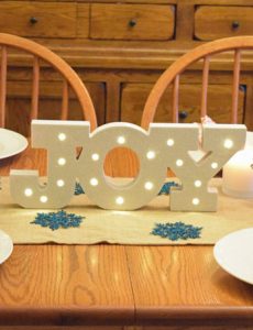 A Christmas table with silver reindeer, a burlap table runner, white lanterns and a lighted marquee joy sign