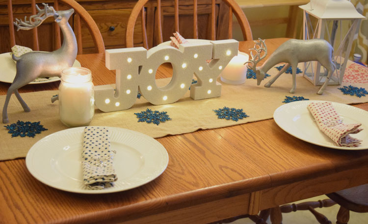 Christmas holiday table with silver reindeer, burlap table runner and lighted Joy marquee sign