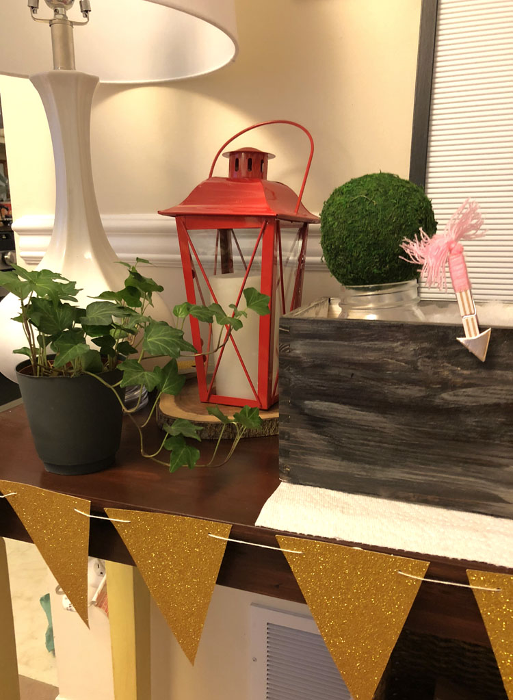 Console table with a red lantern, planter box with mason jars and moss and a gold pennant banner