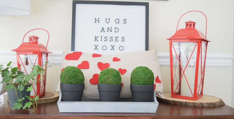 Valentne's Day console table with burlap heart pillow, red lanterns, letter board, gray trayb potted moss and English ivy