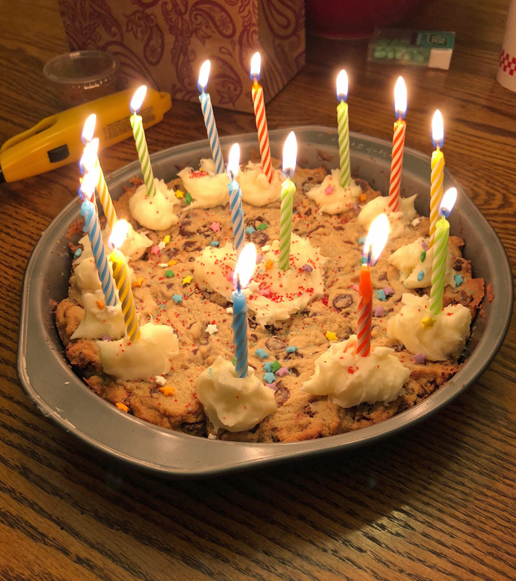 a homemade chocolate chip cookie cake lit with birthday candles