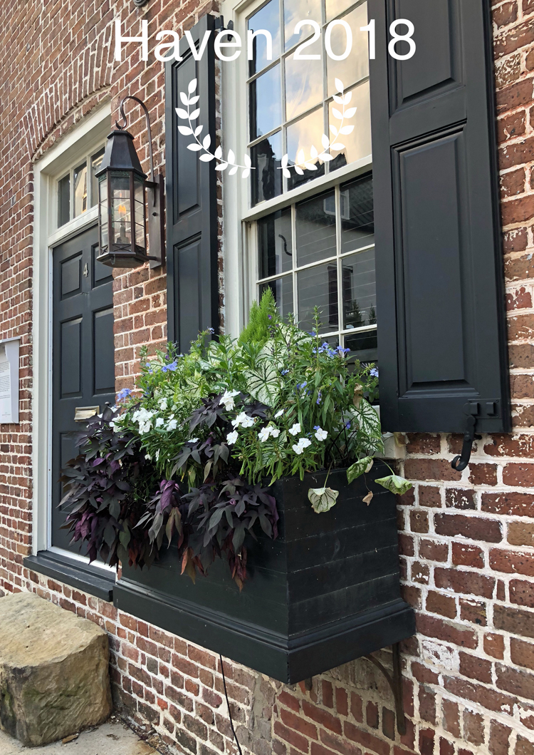 Brick home in Charleston, S.C., with a gas light, black door, black shutters and a beautiful flower box