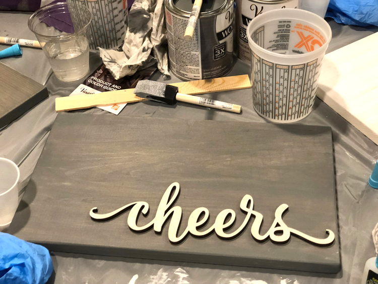 DIY cheers sign made by staining a plank of wood and a word cut-out with Rustoleum quick drying stain