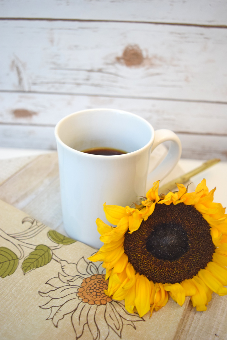 a cup of coffee with a fall sunflower against a farmhouse style wall