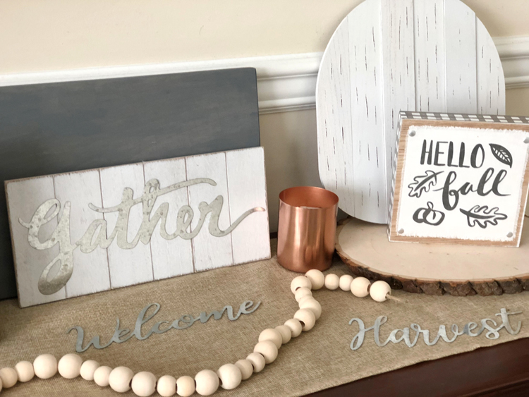 console table with hello fall and gather signs, wood round, copper candle and natural wood bead garland on a burlap table runner