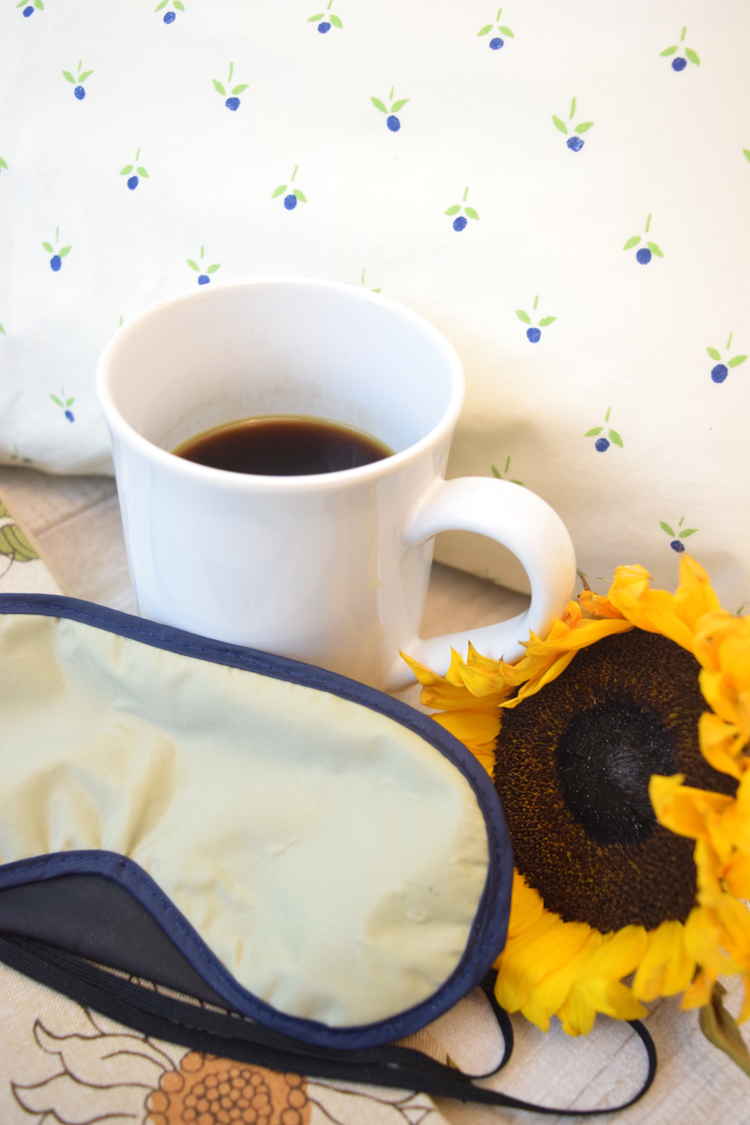 Cup of coffee with sleep mask and sunflower against a pillow