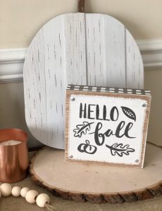Hello sign on an autumn console table on a wood round and in front of a white wooden pumpkin