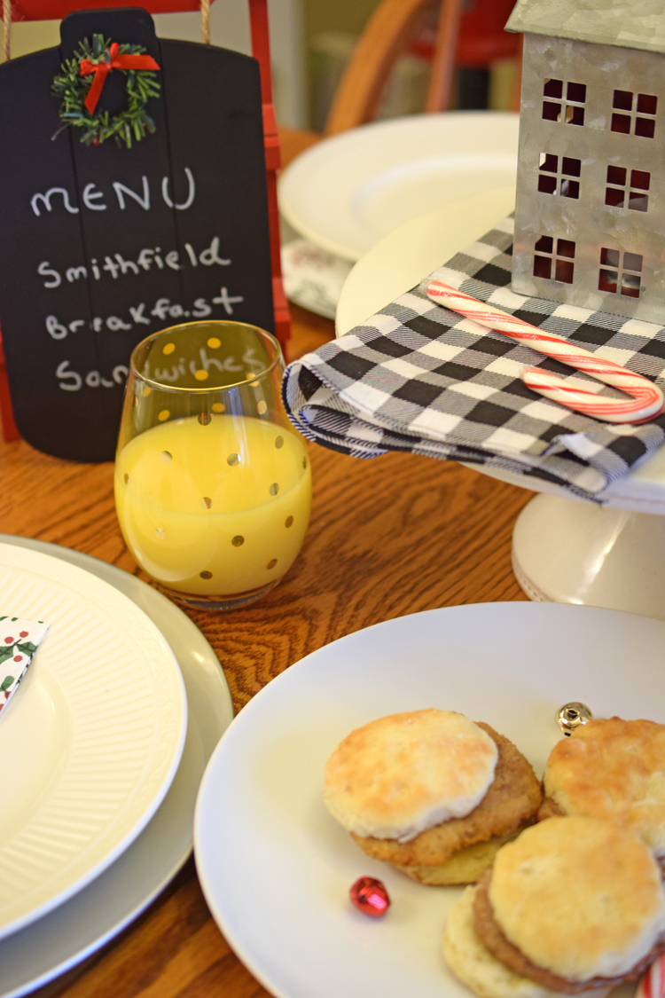 A cute holiday table with a chalkboard menu, buffalo plaid napkins, orange juice and Smithfield Breakfast sandwiches