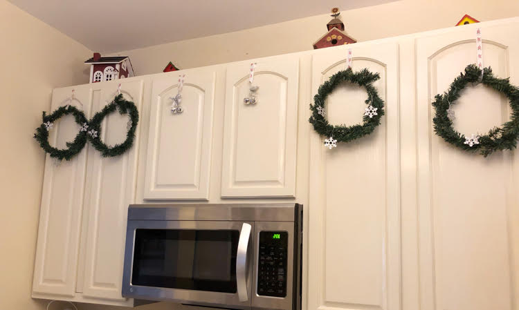 Faux Christmas wreaths hung on white kitchen cabinets with ribbon