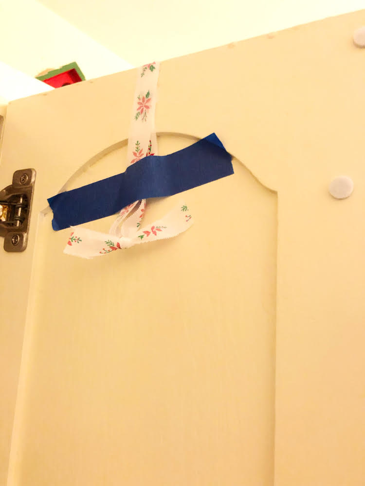 All you need is simple painter's tape to hang a lightweight faux dollar store wreath on kitchen cabinets