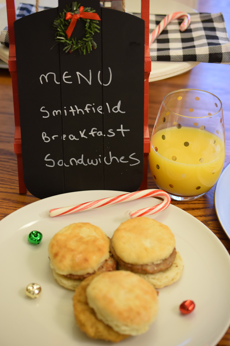 A Christmas holiday table set with juice, breakfast sandwiches and a cute chalkboard menu