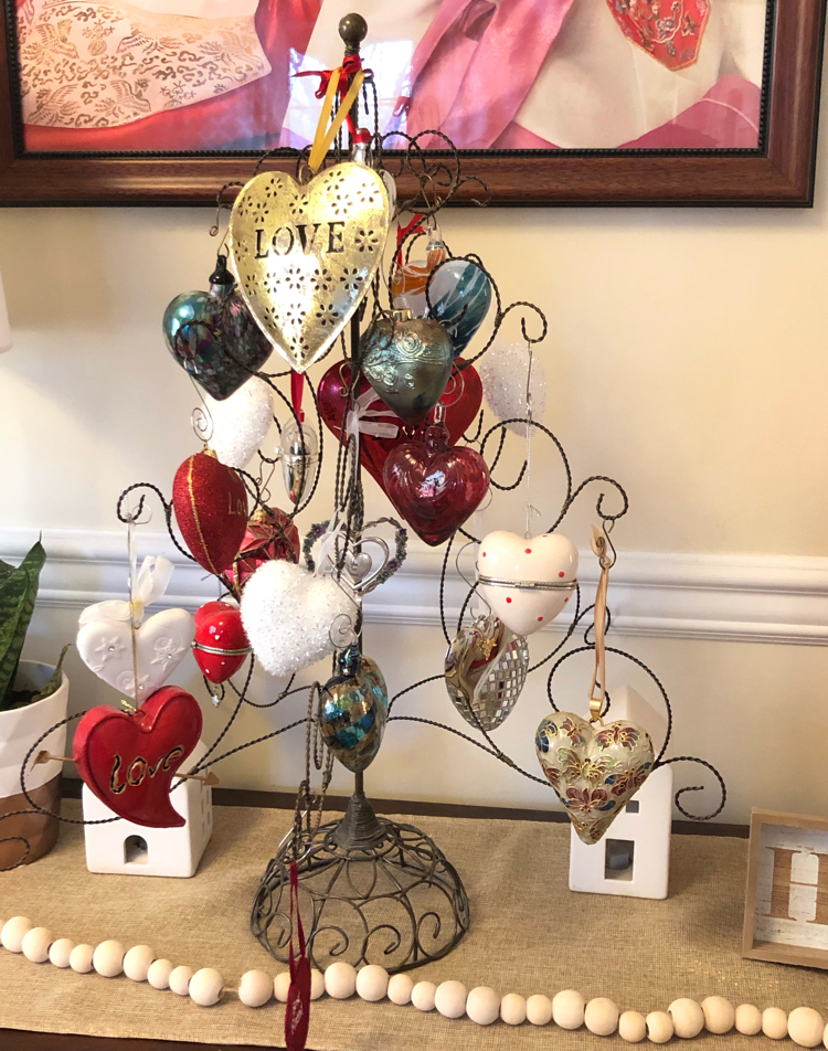 Console table decorated for Valentine's Day with a heart ornament tree, heart ornaments, white ceramic houses and a potted snake plant