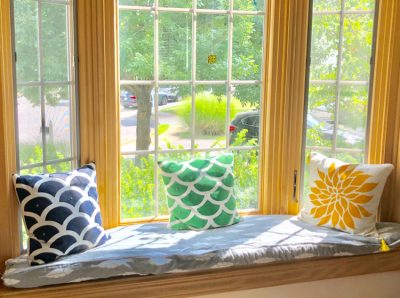 A window seat with a DIY boxed cushion with piping. Also shown are DIY stenciled pillows.