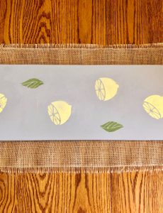 A DIY wooden table runner stenciled with lemons using DecoArt Americana Chalky Finish Paints