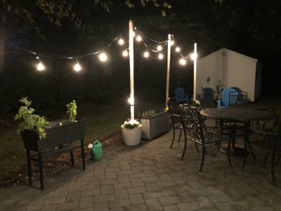 A paver patio lit at night with DIY planter string light poles and string lights.