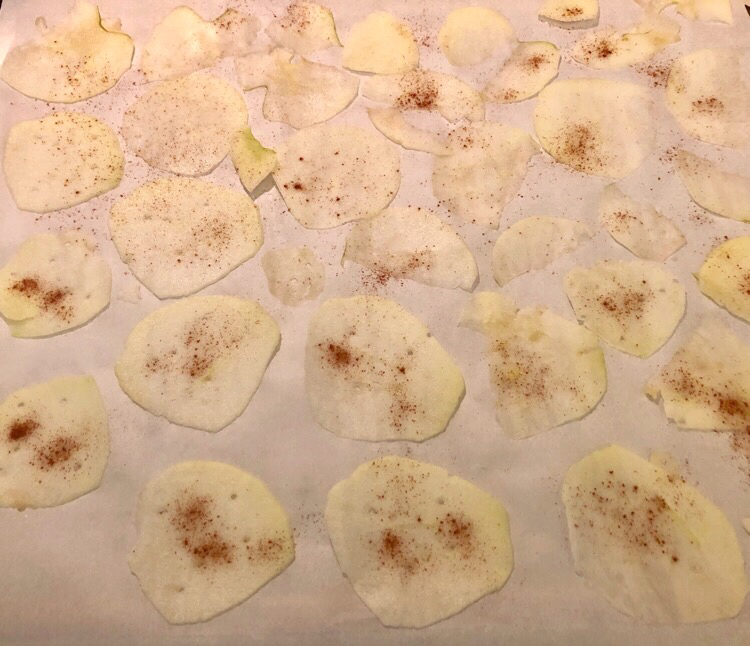 apple slices spread on a sheet of parchment paper to be baked