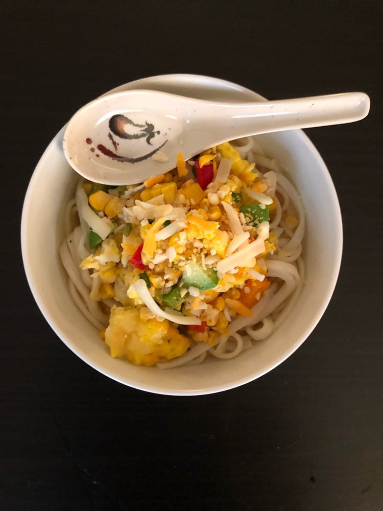 chicken garlic udon soup topped with cheesy scrambled eggs and peppers, onions, corn and avocado