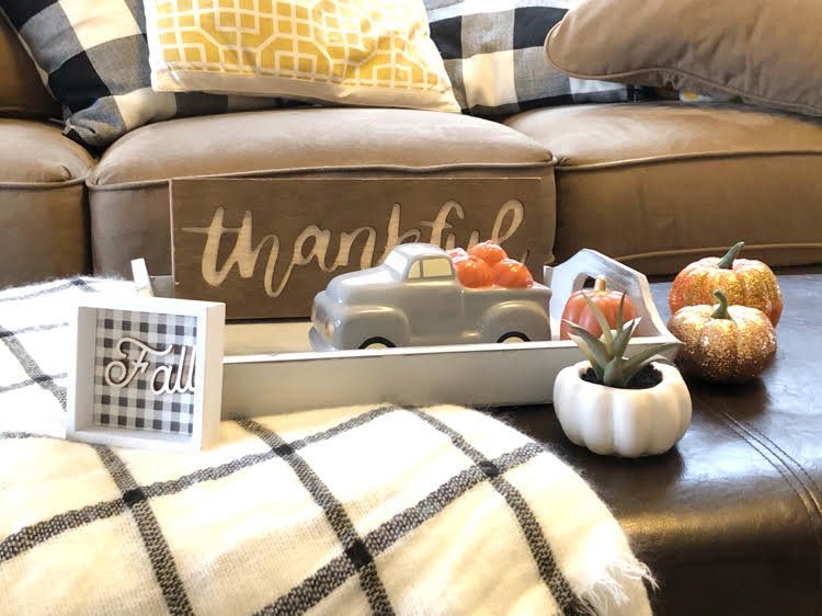A closeup of farmhouse-style decorated coffee table with a mini pickup truck, fall and Thanksgiving signs and faux pumpkins