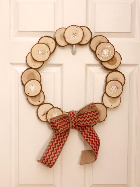 A wood wreath made by gluing wood slices to a large embroidery hoop and adding a homemade burlap wreath