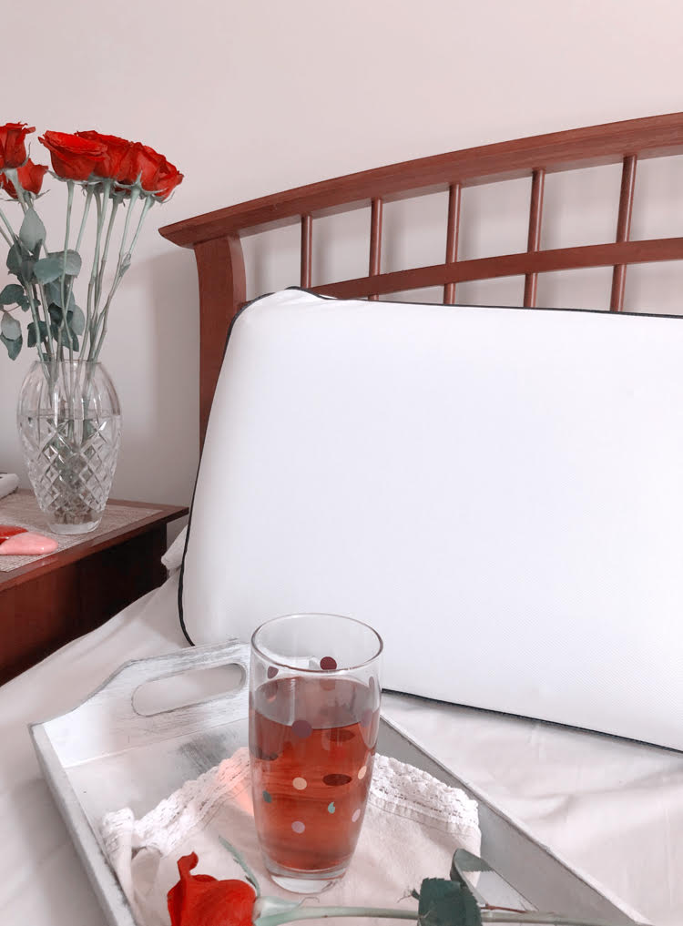 A farmhouse style bed with a cooling memory foam pillow. A vase of roses on a nightstand. A tray with a glass of iced tea.