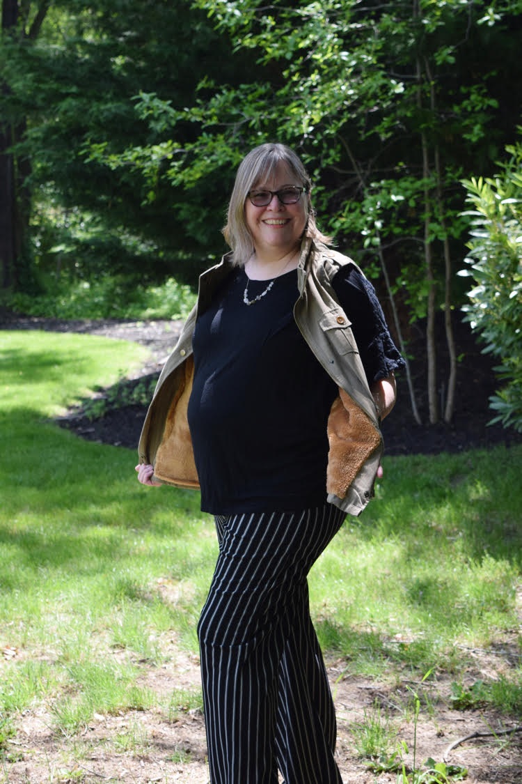 A woman wearing a faux fur lined utility vest with a pair of wide legged black and white striped pants.