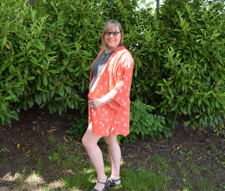 Woman wearing a grey T shirt, a peach kimono with a cacti print and gray sandals.