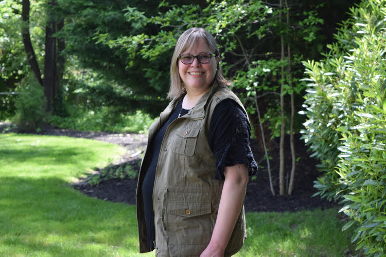 A woman models an olive colored utility vest in a backyard