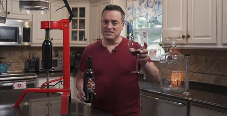 Mario Asaro, founder of Theme Night Wines, in a white kitchen with a bottle of wine