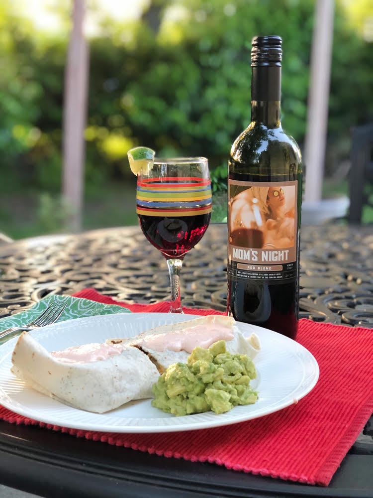 A glass of Mom's Night red wine with a plate that holds a quesadilla and fresh guacamole on an outdoor table.