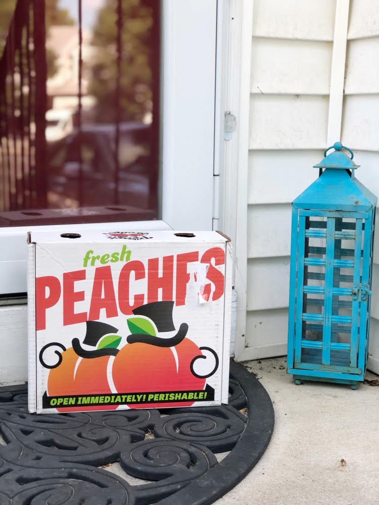box of fresh peaches from The Peach Brothers by a red front door