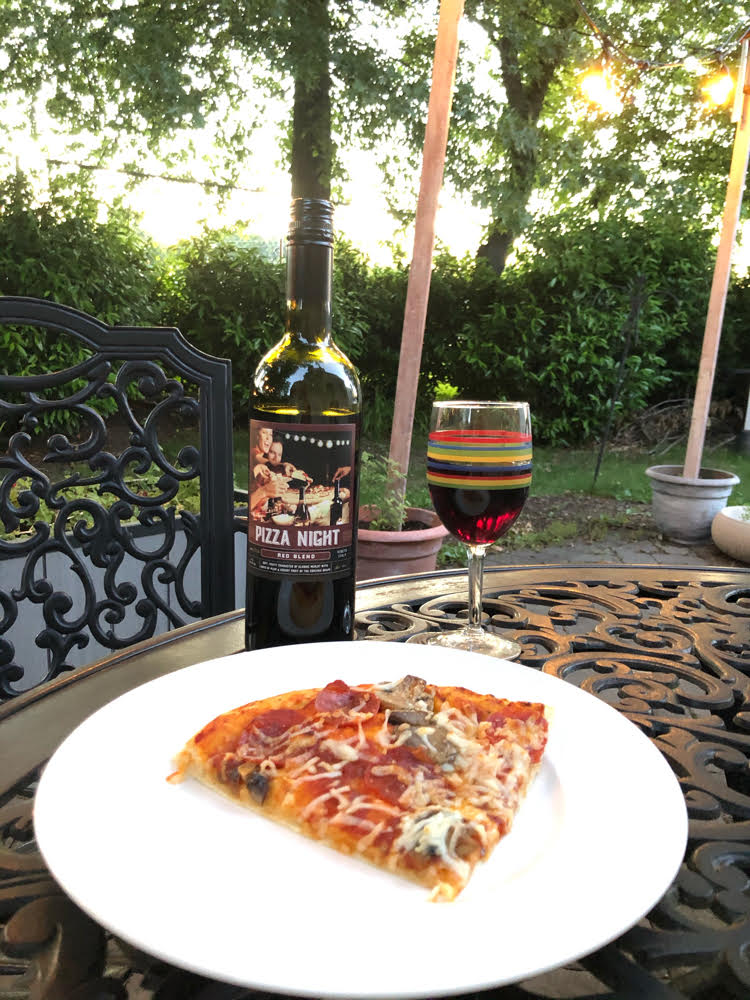 Pizza Night wine with a slice of pepperoni and mushroom pizza on a wrought iron patio table.