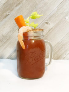 a mason jar glass of Bloody Mary with shrimp, carrot and celery