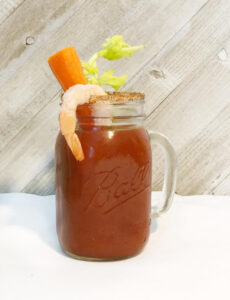 a mason jar glass of Bloody Mary with shrimp, carrot and celery