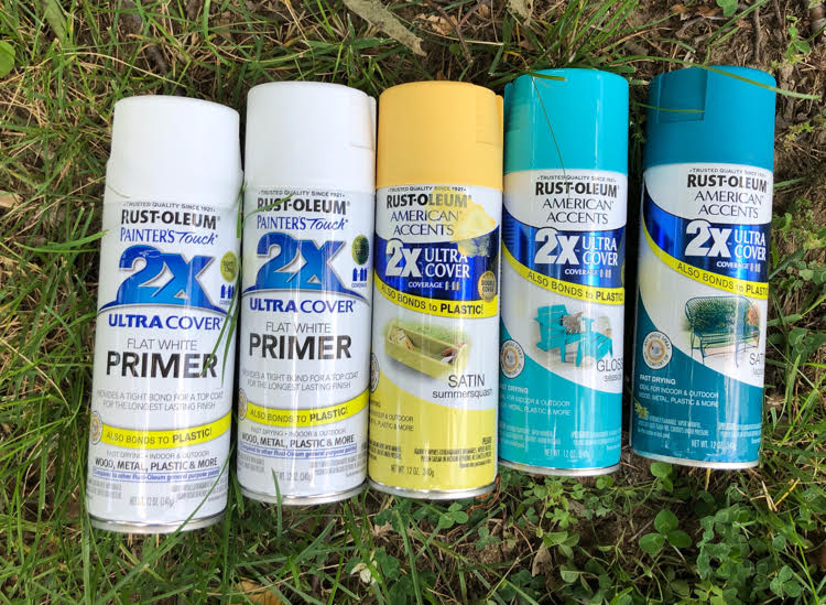 Cans of white, yellow and blue spray paint on green grass