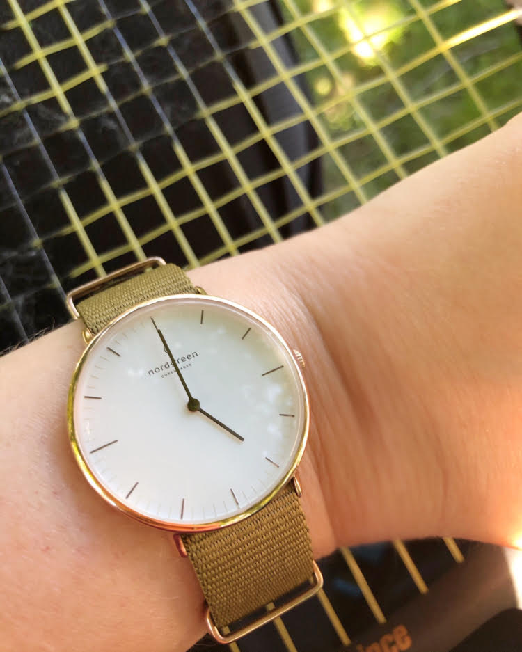 Pretty Nordgreen watch with a white face and a green nylon strap against a tennis racket