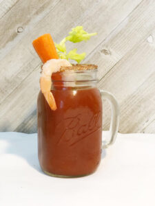 A Bloody Mary in a Ball Jar with a carrot and celery stick and a cooked shrimp