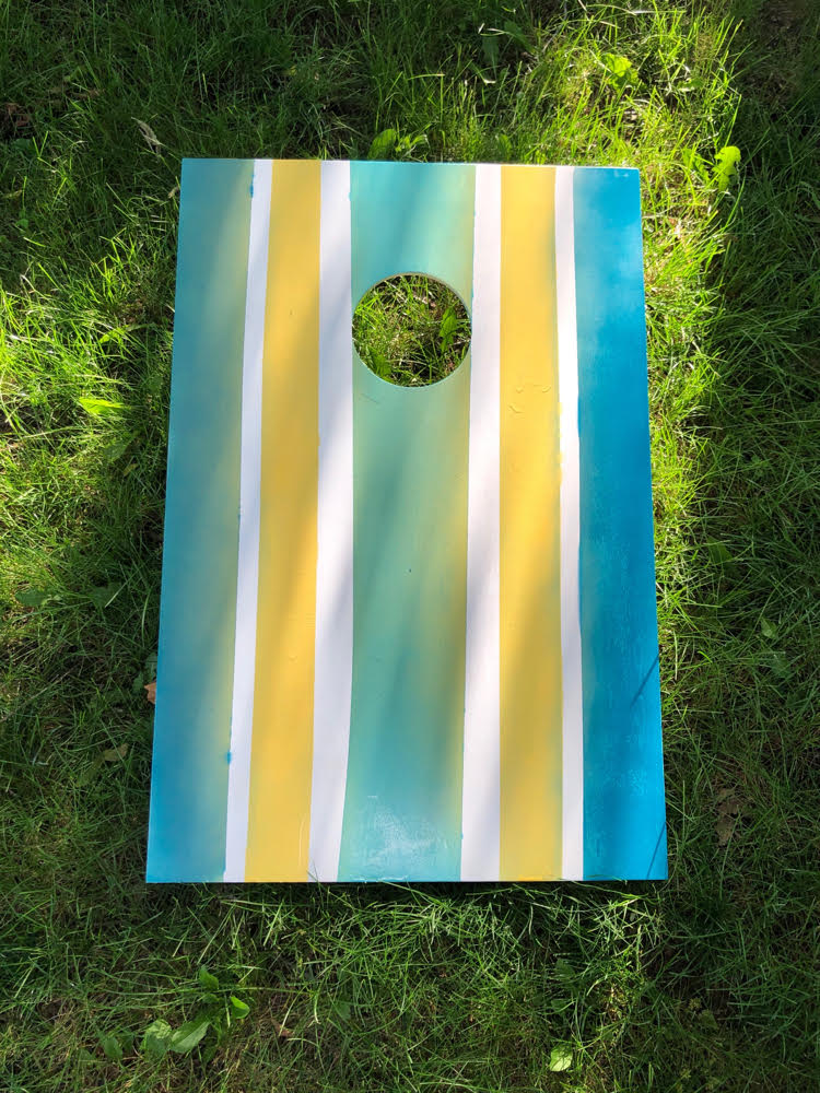 corn hole board spray painted with green, yellow and blue stripes