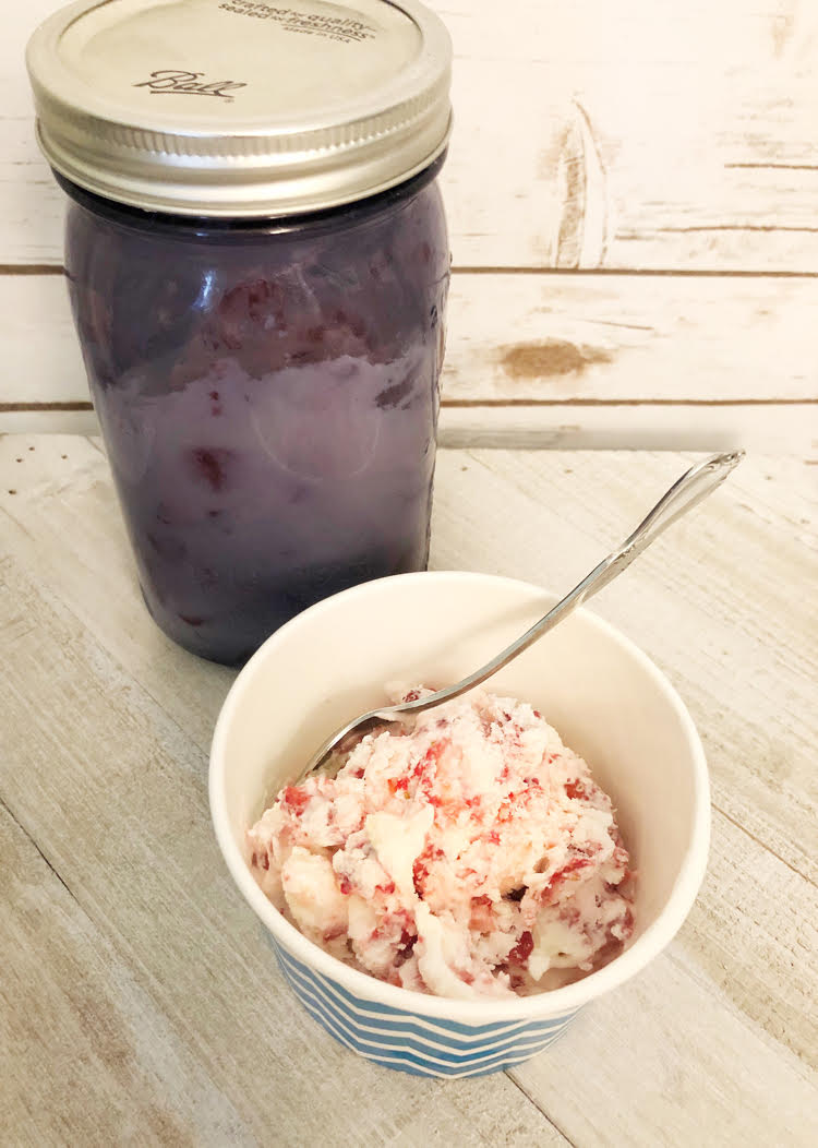 homemade ice cream in a chevon paper cup in a front of a purple Ball mason jar filled with homemade strawberry ice cream