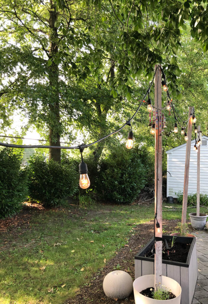 a gray paver patio with Edison style patio string lights strung on DIY planter string light poles