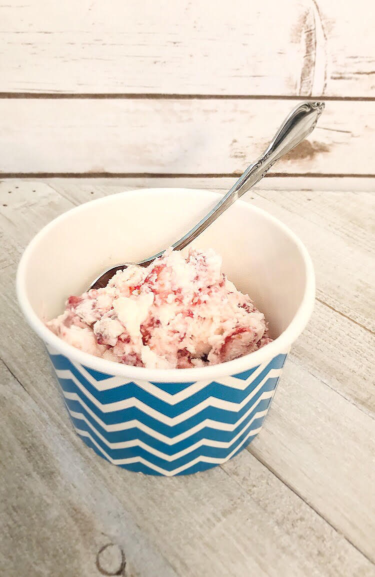 Homemade strawberry ice cream in a chevron print paper cup on a faded gray wood surface