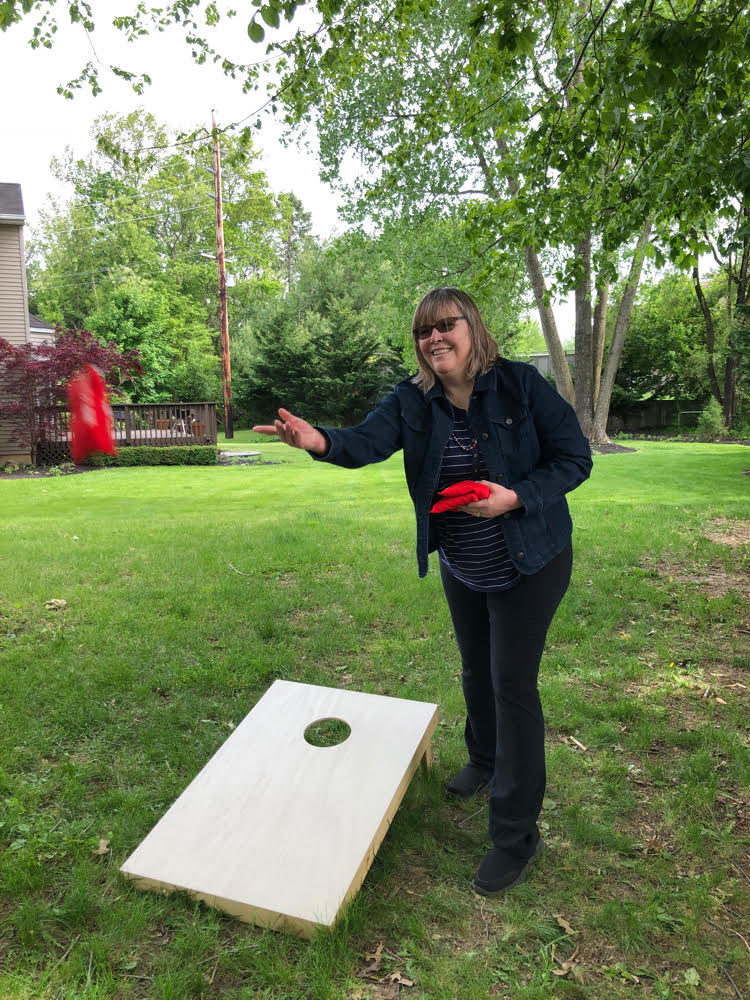 Lauren of Mom Home Guide tosses a bean bag while standing by a corn hole board.