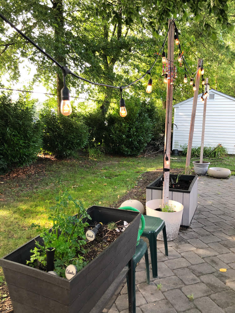 Gray paver patio with DIY string light posts and a raised garden